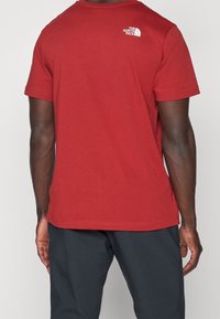 Red cotton t-shirt with short sleeves and a crew neck. Features a small white logo on the upper back. Smooth texture, relaxed fit.