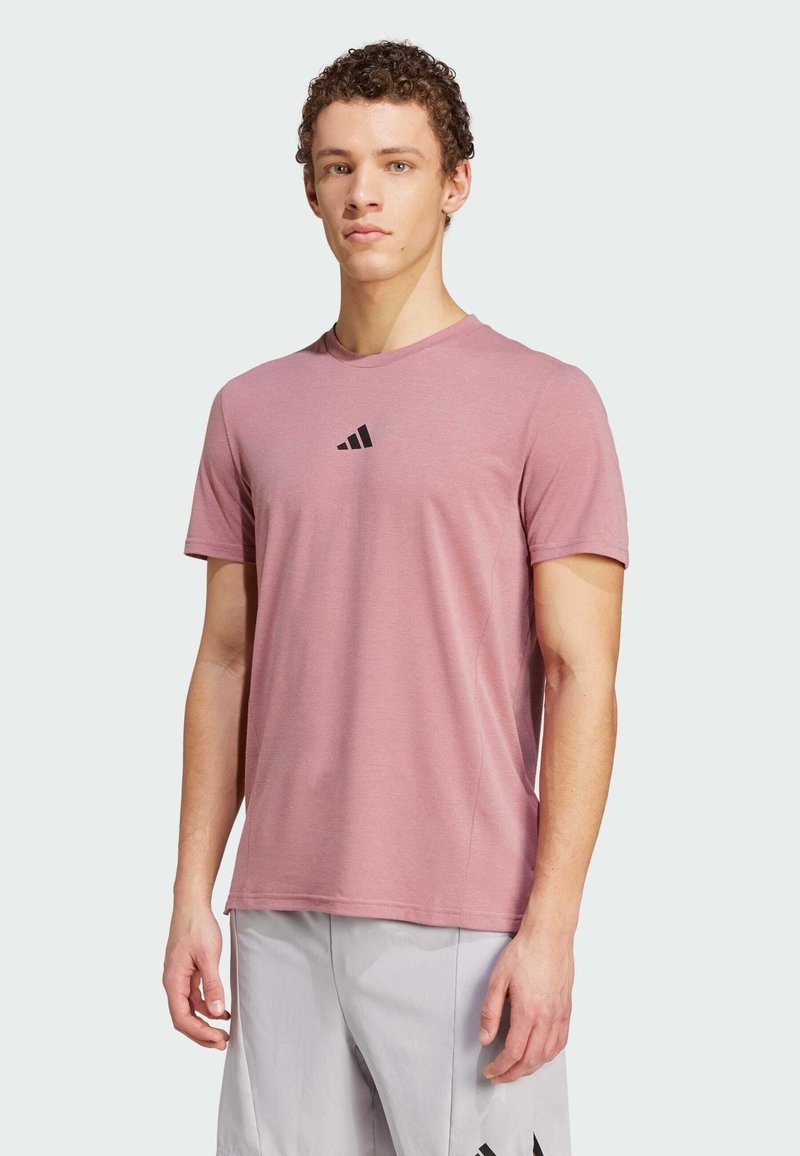 T-shirt de sport léger à manches courtes, rose, avec un logo noir sur la poitrine. Design col rond, texture lisse et coupe décontractée.