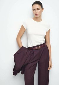 T-shirt blanc à manches courtes associé à un pantalon taille haute bordeaux foncé, rehaussé d'une ceinture marron avec une boucle dorée.