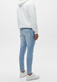 Světlé modré roztrhané džíny s úzkým střihem, s třepenými lemy a zadními kapsami, nošené s bílou mikinou s kapucí a bílými teniskami.