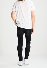 Svarta slim fit jeans med låg midja, detaljerad sömnad på bakfickorna och en slät yta; kombinerat med en enkel vit t-shirt.