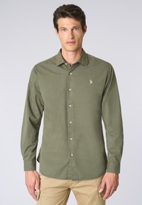 Camicia a maniche lunghe verde oliva con colletto button-down, dotata di bottoni frontali e di un piccolo emblema ricamato sul petto.