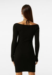 Černé žebrované pletené šaty s dlouhými rukávy, výstřihem přes ramena a šňůrkou vzadu. Příjemně přiléhavý střih a délka do poloviny stehen.