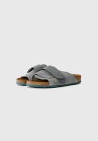 Sandales à brides croisées en suède gris avec une semelle intermédiaire en liège et une semelle en caoutchouc turquoise. Dotées d'une bande Velcro pour un ajustement réglable.