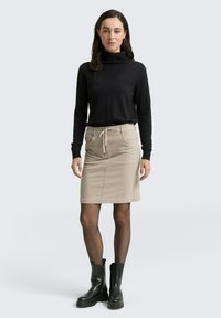 Jupe beige longueur genou avec taille élastique, associée à un col roulé noir à manches longues et des bottines noires.