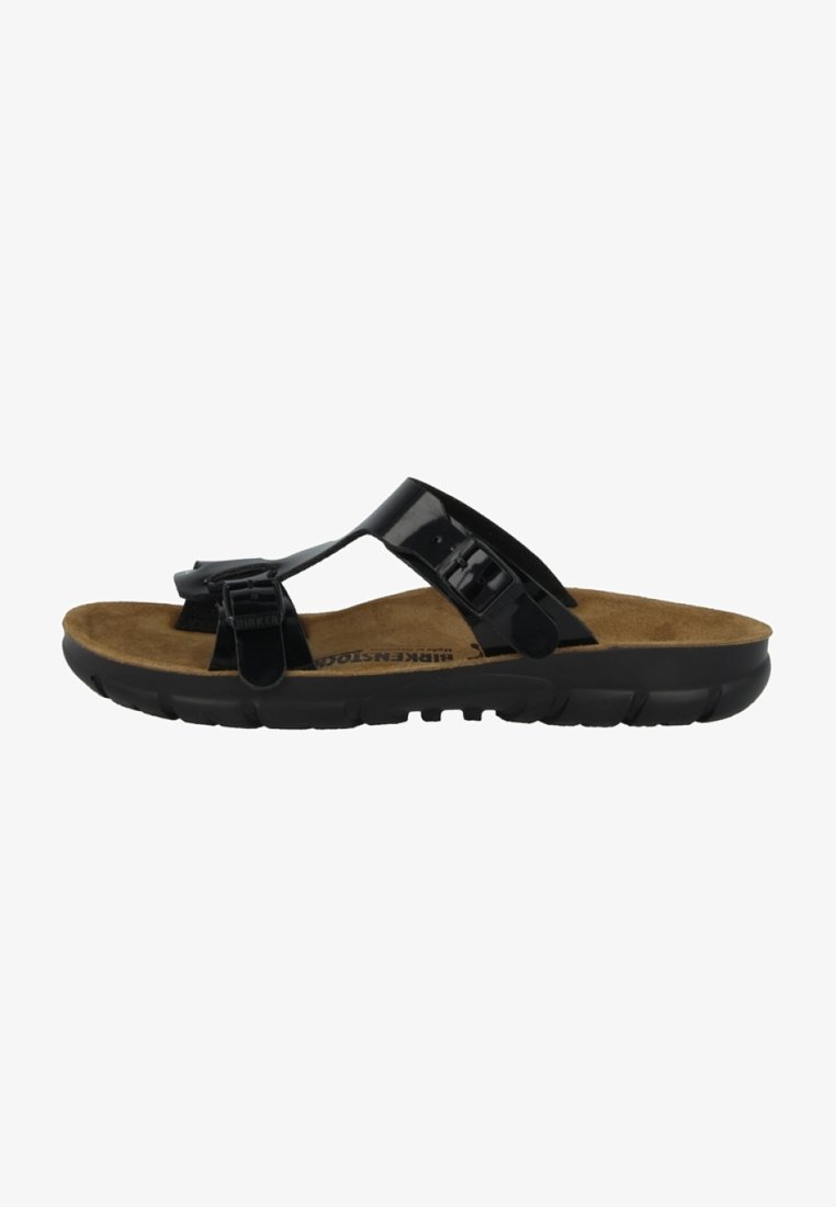 Black sandal with glossy synthetic straps, cork footbed, and a black rubber sole featuring grooves for traction. Buckled details on straps.
