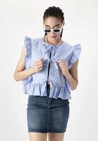 Blouse à manches courtes bleu et blanc à rayures avec des bords volants et un col noué, associée à une mini-jupe en denim.