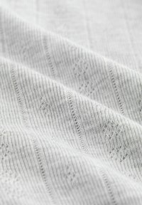 Tessuto lavorato a maglia grigio chiaro con sottili righe verticali e motivi a diamante. Texture morbida, leggermente elastica e cuciture finemente dettagliate.