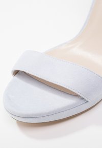 Sandale à talons en suede bleu clair, présentant une large bande unique sur le bout et une boîte à orteils lisse et arrondie.