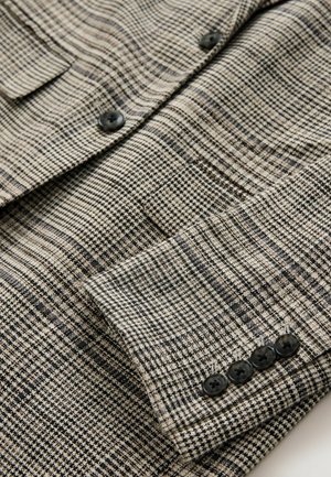 Leichter, strukturierter Blazer in einem schwarz-beigen Karo-Muster, mit vier schwarzen Knöpfen am Ärmel und einer Brusttaschen-Detail.