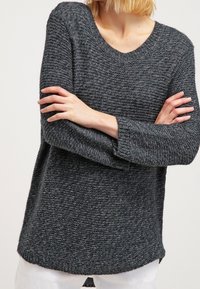 Mörkgrå stickad tröja med rund halsringning, långa ärmar och en texturerad yta. Har en lätt rundad fåll.