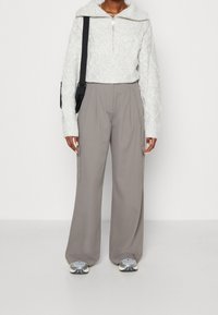 Lichtgrijze kabelgebreide trui met een brede kraag en een halve rits, gecombineerd met losvallende beige cargobroek met zijzakken.