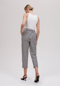 Un débardeur blanc à côtes associé à un pantalon cropped rayé bleu marine et blanc. Le pantalon possède une taille élastique et des ourlets retroussés. Escarpins noirs.