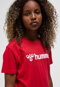 Röd bomullst-shirt med vitt "hummel"-logotyp och bikoncept. Kort ärm och rund hals, slät textur.