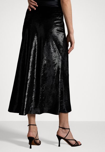 Black, flowing midi skirt in shiny, soft fabric with a smooth texture. Worn with strappy black heels, showing a fitted waistline.