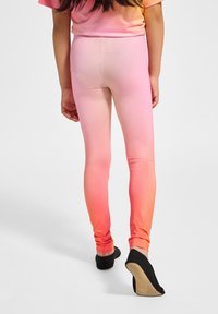 Roze ombre legging die van licht naar donker overgaat, gemaakt van rekbaar materiaal, gecombineerd met zwarte platte schoenen. Glad materiaal, strakke pasvorm.