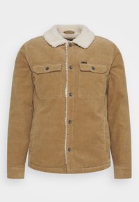 Brązowa kurtka z korduroy z kremowym kołnierzem sherpa, dwoma przednimi kieszeniami z klapami i zapięciami na guziki. Miękka tekstura i prosty krój.