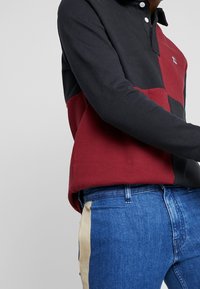 Långärmad pikétröja med en färgblockdesign i mörk marinblå och bordeaux, med en knappkrage och ribbad textur. Kombinerad med denimjeans.