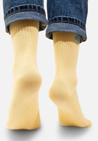 Żółte, prążkowane skarpetki o miękkiej teksturze, z jasnoniebieskim wzorem w okolicy kostki, noszone z podwiniętymi niebieskimi dżinsami.