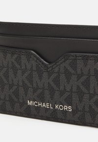 Porte-cartes noir en tissu texturé avec un motif logo entrelacé, rehaussé de finitions en cuir lisse et d'un nom de marque métallique.