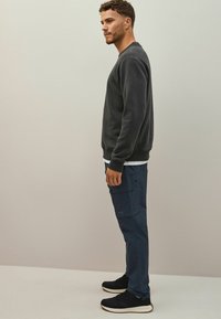 Mörkgrå sweatshirt med texturerad tyg, kombinerad med marinblå cargobyxor med flera fickor och en slät yta. Svarta sneakers fulländar stilen.