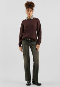 Bordowy sweter o fakturze w połączeniu z szarą koszulą w kratę, zestawiony z prostymi ciemnymi dżinsami i czarnymi botkami za kostkę.