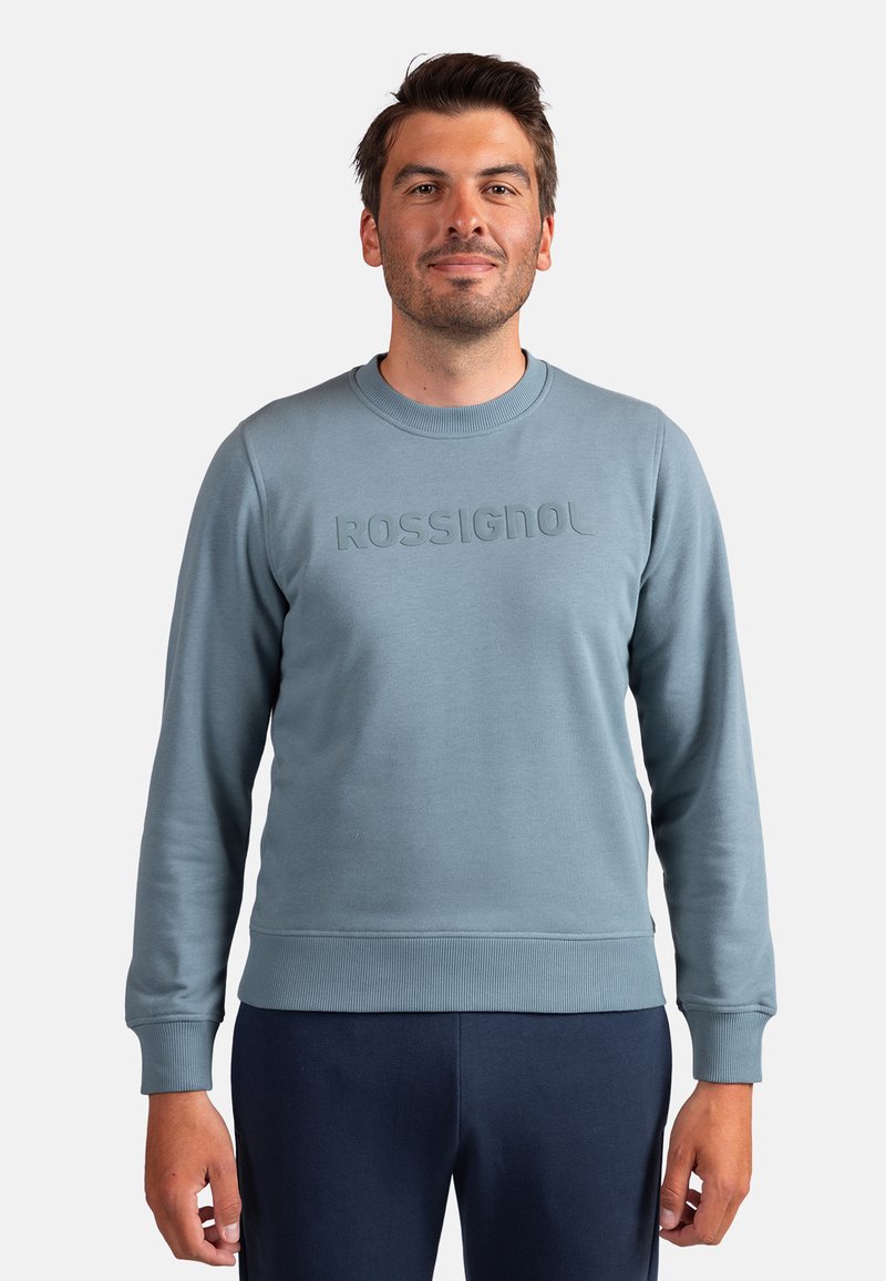 Sudadera azul claro con puños y dobladillo acanalados, con un logo en relieve de "ROSSIGNOL" en el pecho. Textura de tela lisa.