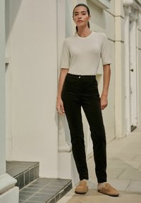 Lichtbeige top met korte mouwen, zwarte strak aansluitende broek en bruine instappers. Glad textuur met een minimalistisch ontwerp en zachte materialen.