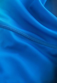 Blauwe stof met een gladde textuur, voorzien van een nette naad met bijpassend garen. Licht glanzend, wat een gradiënt effect creëert.