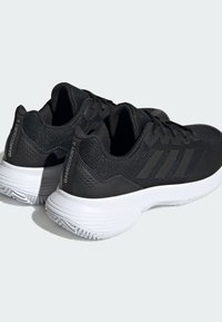 Scarpe da ginnastica nere con tomaia in maglia; presentano tre strisce scure, colletto imbottito e suola in gomma bianca con battistrada testurizzato.