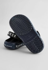 Mørkeblå gummisandaler med en struktureret sål, der har sorte stropper med hvid "BAKER" tekst og en glat overflade.