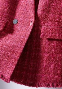 Punainen teksturoitu bleiseri, jossa on kudottu kuvio, hopeiset napit ja rispaantuneet helma-yksityiskohdat. Kankaassa on rikas, kaksivärinen ilme.