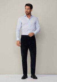 Camicia a strisce blu chiaro con bottoni abbinata a pantaloni in corduroy neri e scarpe in pelle nere. Tessuto liscio, vestibilità su misura e design classico.