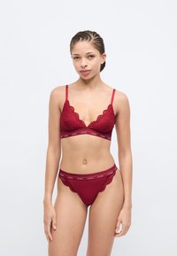 Burgundy lace bralette with scalloped edges and thin straps, paired with matching lace-trimmed thong featuring an elastic logo waistband.