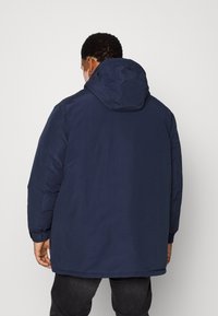 Mörkblå puffjacka med huva, med elastiska ärmslut och justerbar fåll. Slät textur, avslappnad design och minimalistisk stil.