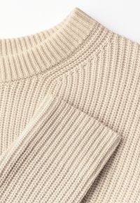 Beige gestrickter Pullover mit einer gerippten Textur. Verfügt über einen hohen Kragen und zwei umgeschlagene Ärmel, die einen weichen und gemütlichen Stoff zeigen.