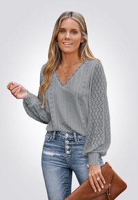 Gray blouse with v-neckline and scalloped edges, featuring eyelet and textured patterns. Paired with distressed jeans and a brown clutch.