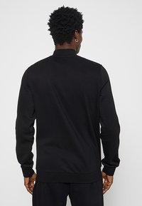 Sudadera negra con cuello redondo, mangas largas, puños y dobladillo acanalados, hecha de un tejido suave. Diseño sencillo, sin patrones o acentos visibles.