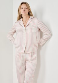 Gestreept pyjamaset in licht crèmekleur met roze strepen. Voorzien van knoopsluiting op het bovenstuk, een borstzak en loszittende broek. Zachte stof.