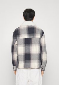 Koszula w kratę w odcieniach szarości, granatu i kremu, z kołnierzem wyłożonym miękkim futerkiem, długimi rękawami i mankietami na guziki.