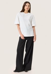 Witte oversized t-shirt met korte mouwen, gecombineerd met hoge, wijde zwarte broeken. Soepele stof, ontspannen pasvorm, minimalistisch ontwerp.