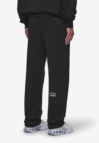 Svarta sweatpants med lös passform. Har en vit logotyp på vänster ben och subtila röda detaljer på midjeresåren. Slät tekstur.