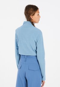 Pullover in pile blu chiaro con colletto alto, design cropped e maniche lunghe, abbinato a pantaloni blu chiaro a vita alta con tasche posteriori.
