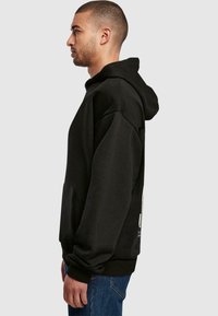 Sort hætte sweatshirt med en løs pasform, blød tekstur og forlommet lomme. Har ribbede manchetter og bund; båret med blå jeans.