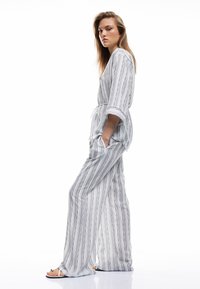 Stribet jumpsuit i lys grå og hvid med brede ben, en indsnævret talje og trekvartærmer, der har sidelommer.