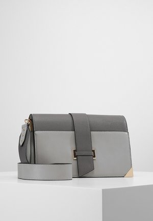 Szarawo-czarna prostokątna torba na ramię z szerokim paskiem, przednią klapką, złotym detalem na rogu i złotą klamrą, umieszczona na białej powierzchni.