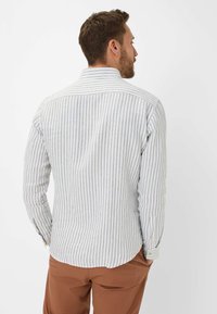 Striped long-sleeve shirt in light colors with thin gray and white stripes, buttoned cuffs, and a curved hem design. Cotton material.