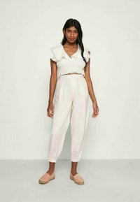 Top branco cropped com mangas com pregas, combinado com calças largas de tom bege claro e sapatos de slip-on rosa. Textura suave, design casual.