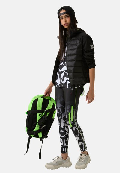 Sort puffjakke, mønstrede sorte og hvide leggings, neongrønne detaljer. Hvide sneakers, sort rygsæk med livlige grønne detaljer.