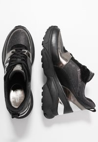 Baskets de sport noires avec accents métalliques, dessus en mesh, semelle rembourrée et surface texturée. Design à lacets avec matériaux contrastants.